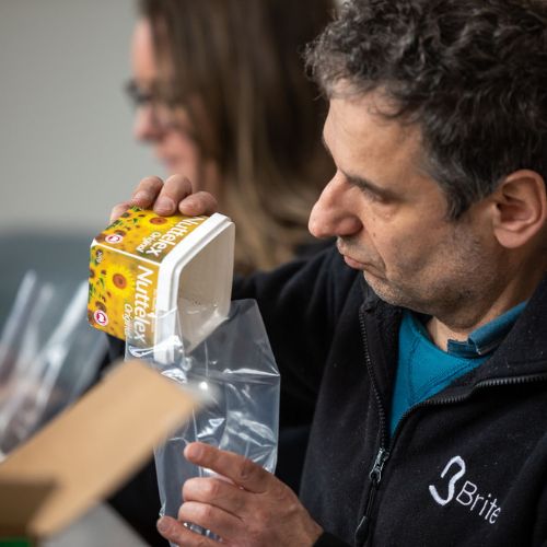 A man is tipping items from a small container into a plastic bag for a client's outsourced kitting service.